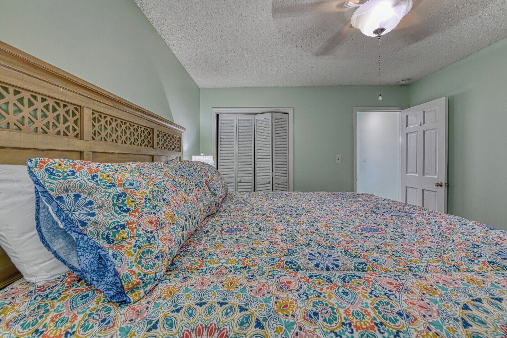 A bedroom with a bed, a ceiling fan, and a door.