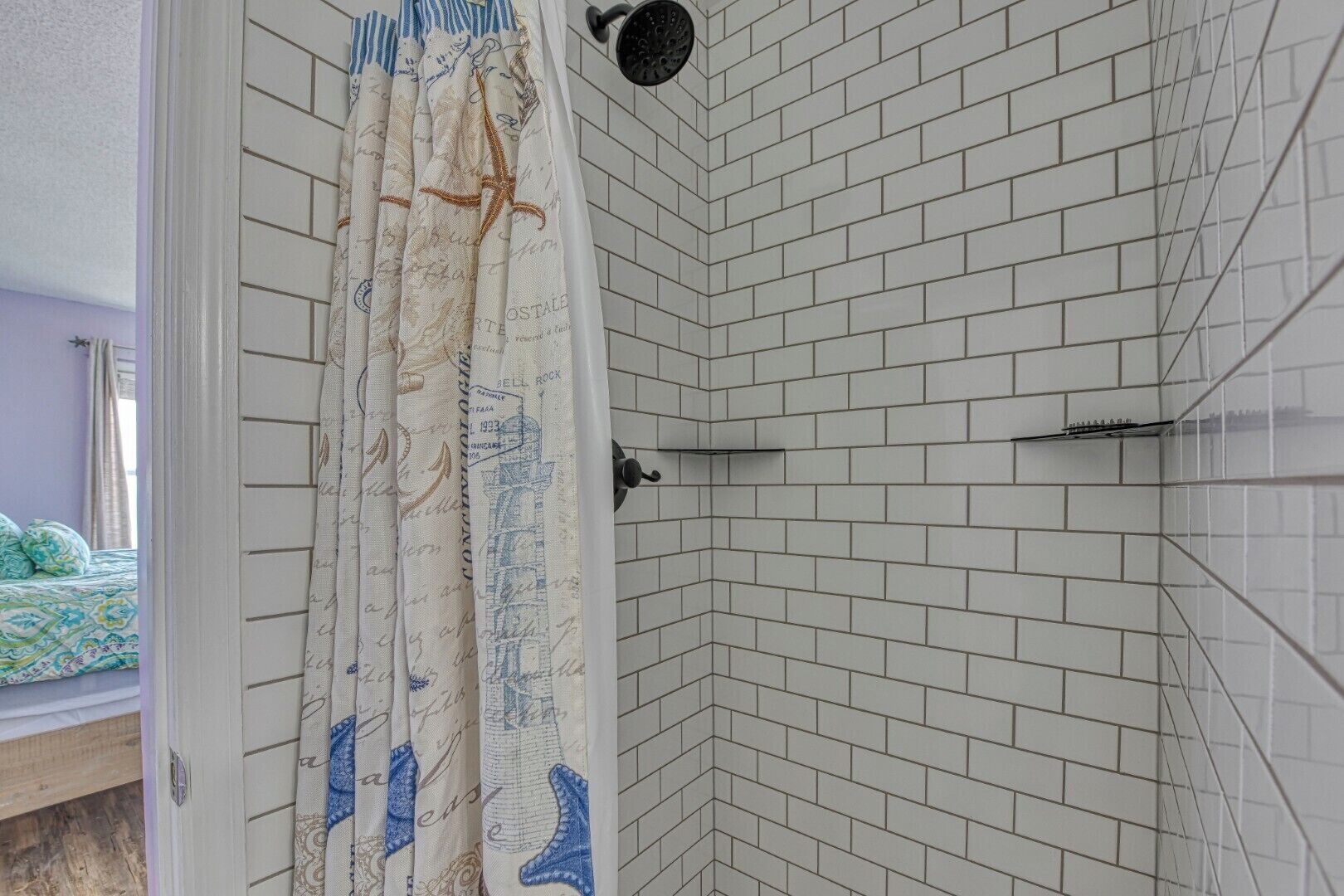Une salle de bain avec des murs recouverts de carreaux blancs, un espace douche et un rideau orné de motifs marins.