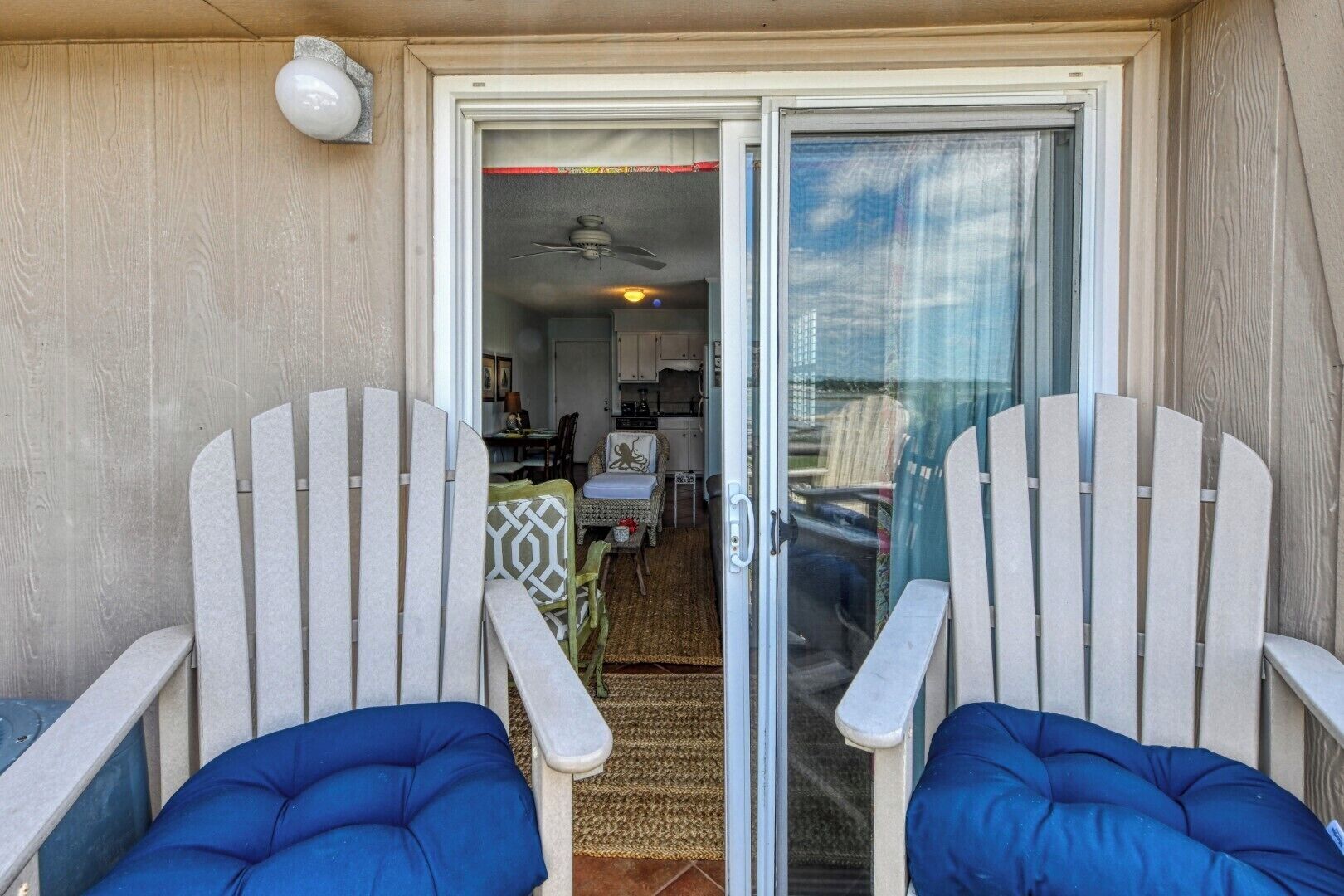 A patio with two Adirondack chairs and a sliding glass door leading to a kitchen area.