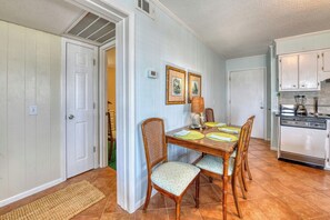 A dining area with a wooden table, four chairs, a lamp, and framed pictures on the wall. - Two Bedroom Condo with a Shared Swimming Pool on the channel front. (Garden City Beach)