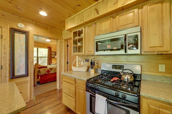 Interior de una cabaña de madera con cocina, que incluye una estufa a gas, un microondas y armarios de madera.
