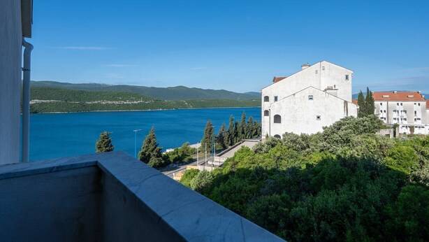 Une vue d’un bâtiment doté d’une grande fenêtre donnant sur une étendue d’eau et des collines.