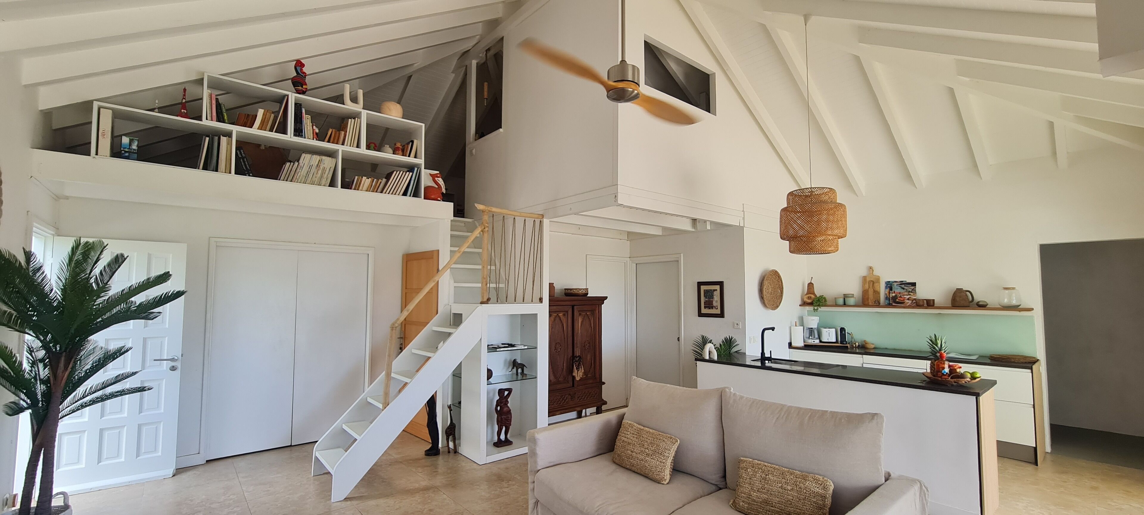Un vaste espace de vie doté d’un haut plafond, d’un escalier menant à une mezzanine, d’un coin cuisine et d’un espace détente avec un canapé.