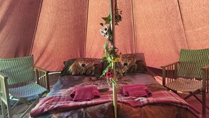 Een gezellige tent met een bed, twee stoelen en een decoratieve plant.