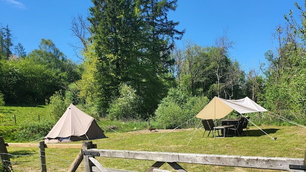Een camping met twee tenten, waarvan er een een tafel en stoelen heeft, en een houten poort met de tekst 'Belt Tent'.