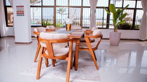 Un coin repas avec une table et des chaises en bois, de grandes fenêtres avec des rideaux et une plante en pot.