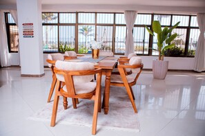 Un comedor con una mesa y sillas de madera, ventanas grandes con cortinas y una planta en maceta.