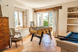 A room with a foosball table, a pool table, a wooden dresser, and a chair.