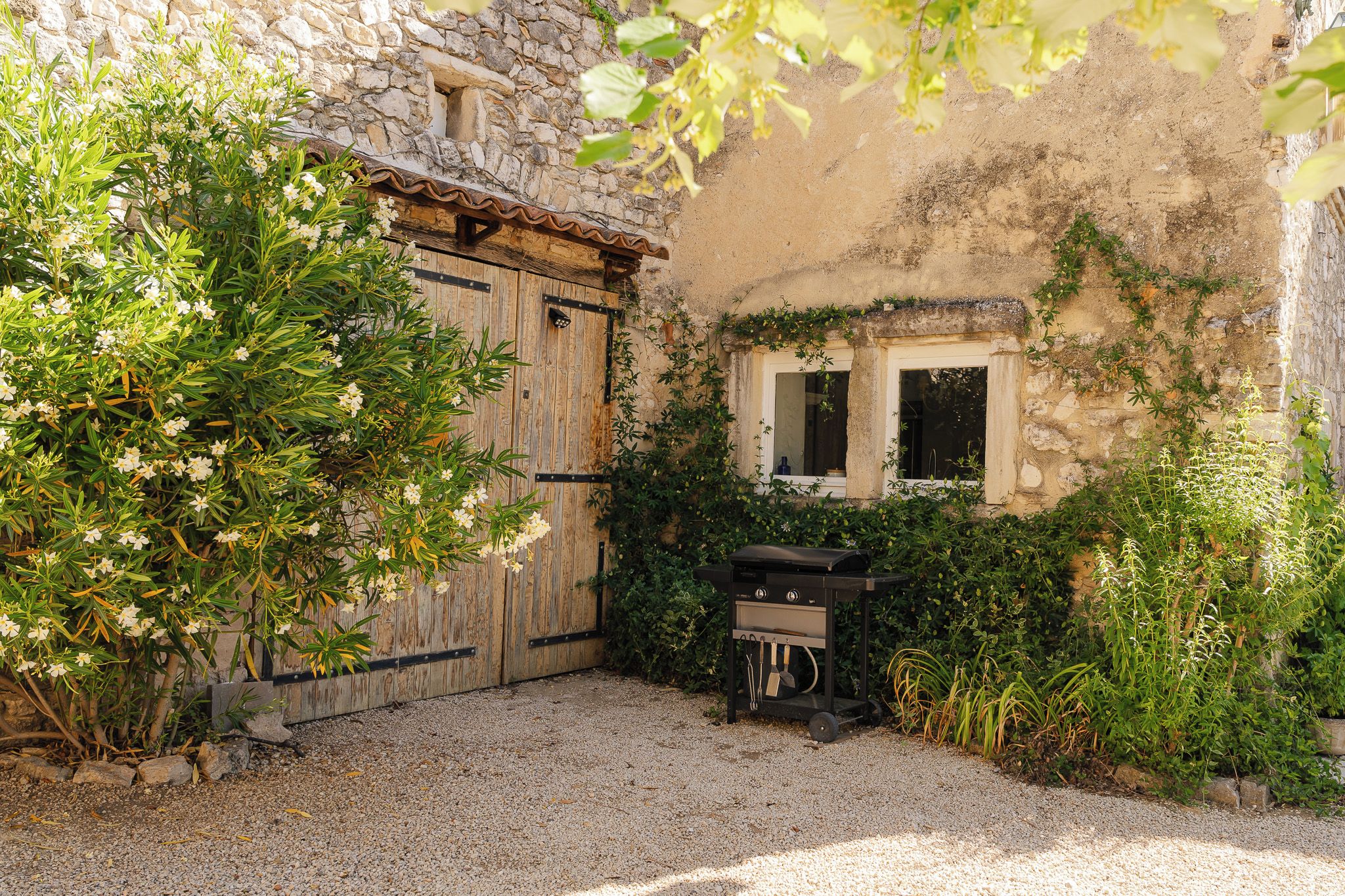 A rustic outdoor area with a gravel ground, a wooden door, a window, and a barbecue grill.