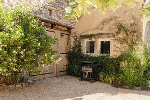 A rustic outdoor area with a gravel ground, a wooden door, a window, and a barbecue grill.
