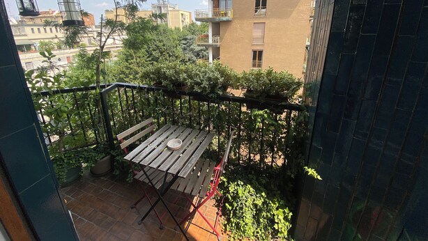 A balcony with a wooden table and chairs, surrounded by greenery and overlooking a residential area with buildings. - Short Rent Milan Porta Vittoria. Studio apartment with balcony (Milano)