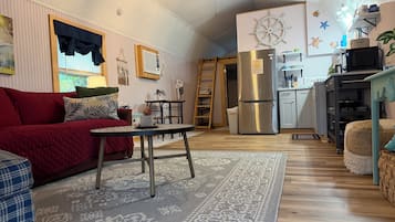 Un salon chaleureux avec un canapé rouge, un tapis à motifs et un coin cuisine doté d’un réfrigérateur en acier inoxydable.