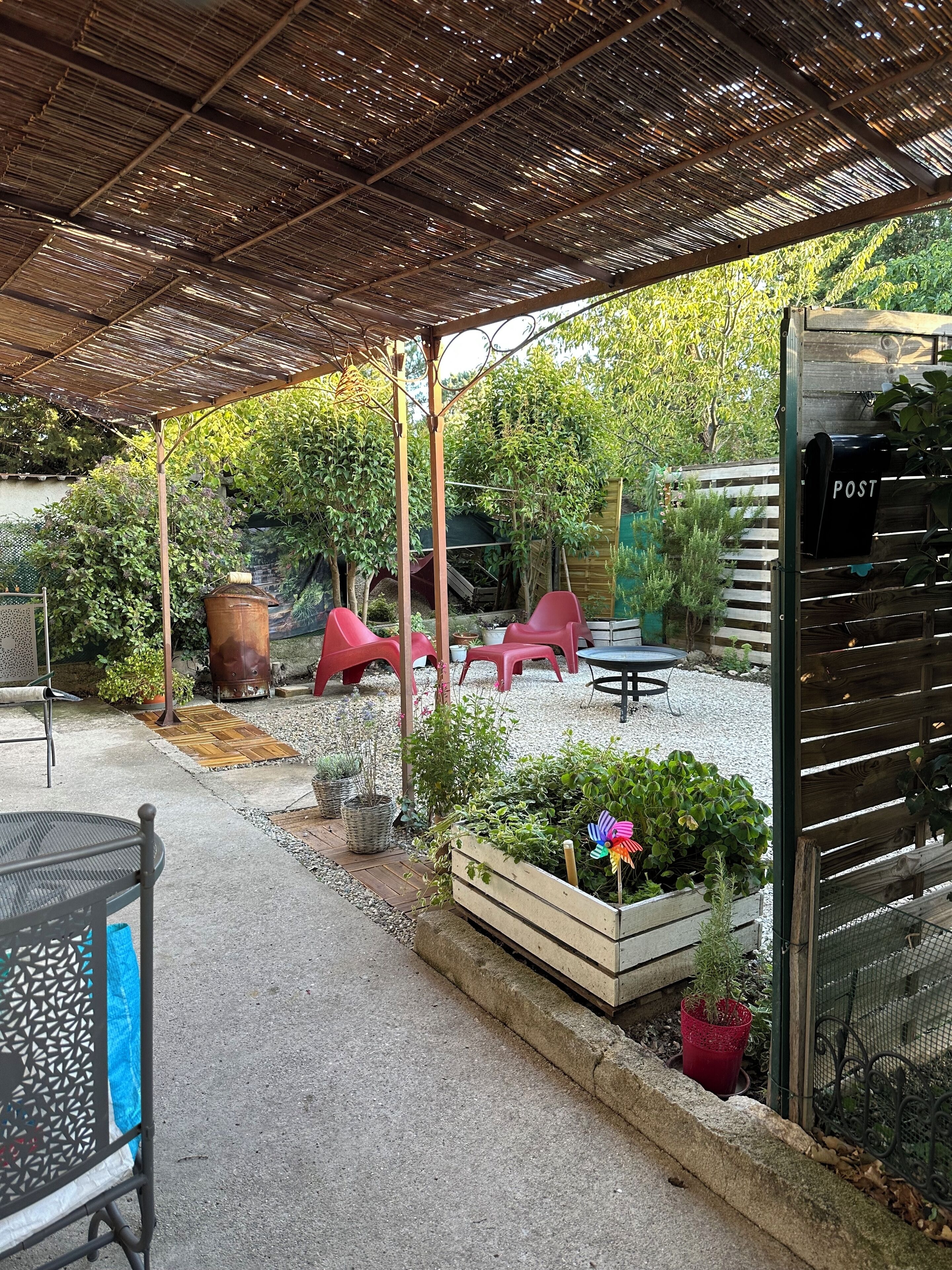 A covered patio area with a pergola, outdoor seating, and a garden with potted plants.
