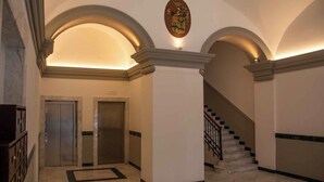Un hall d’entrée avec deux ascenseurs, un escalier et un blason sur le mur.