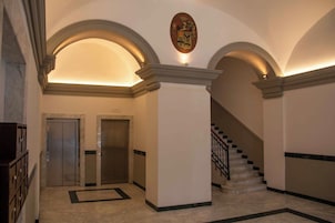Eine Empfangshalle mit zwei Aufzügen, einer Treppe und einem Wappen an der Wand.