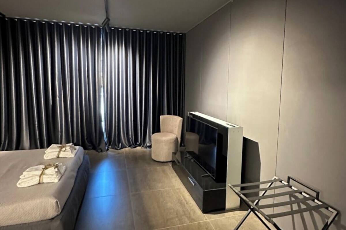 A modern hotel room with a bed, a seating area, a TV, and a drying rack.