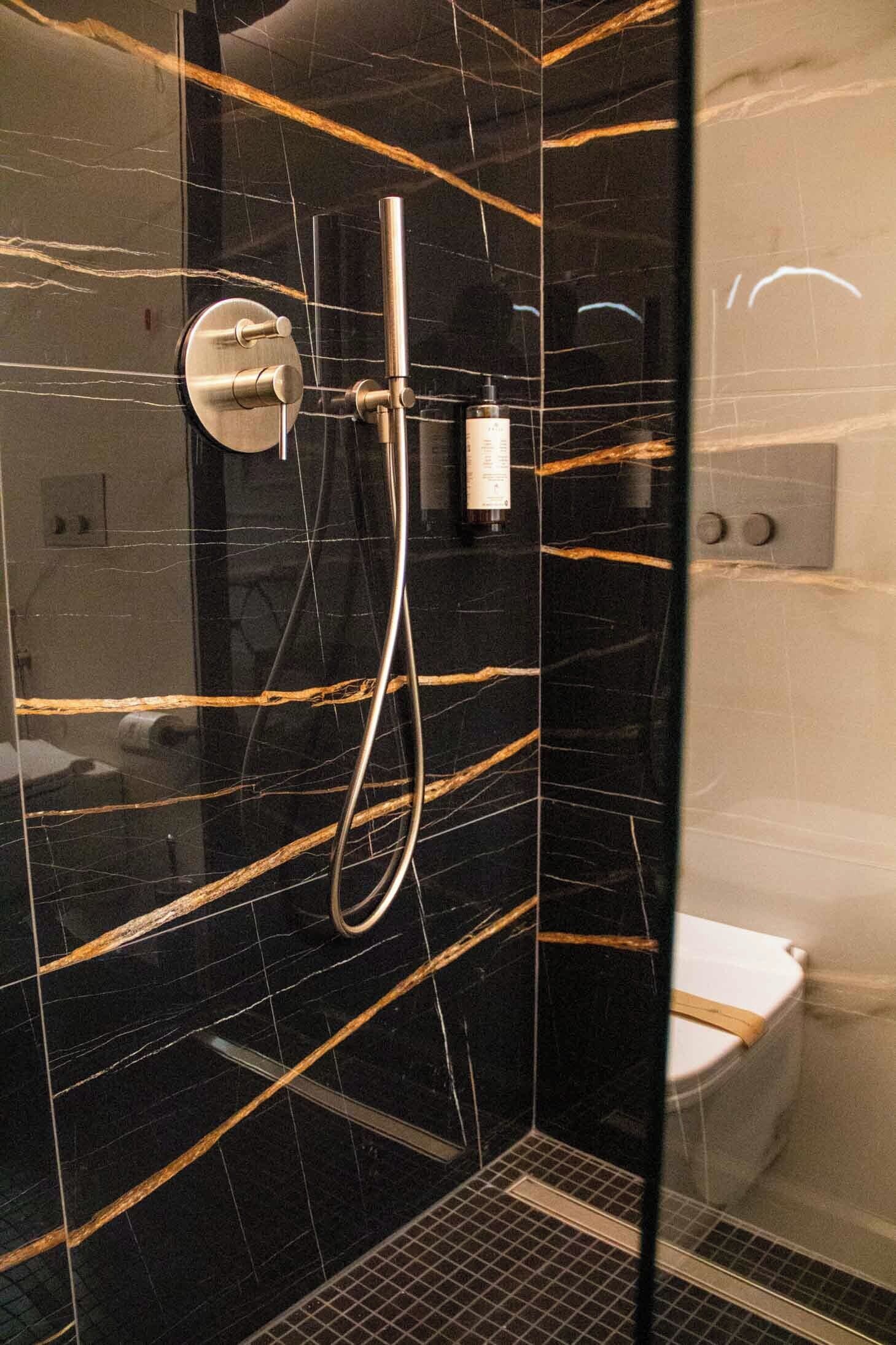 A modern bathroom with a glass-enclosed shower, black marble walls, and a white toilet.