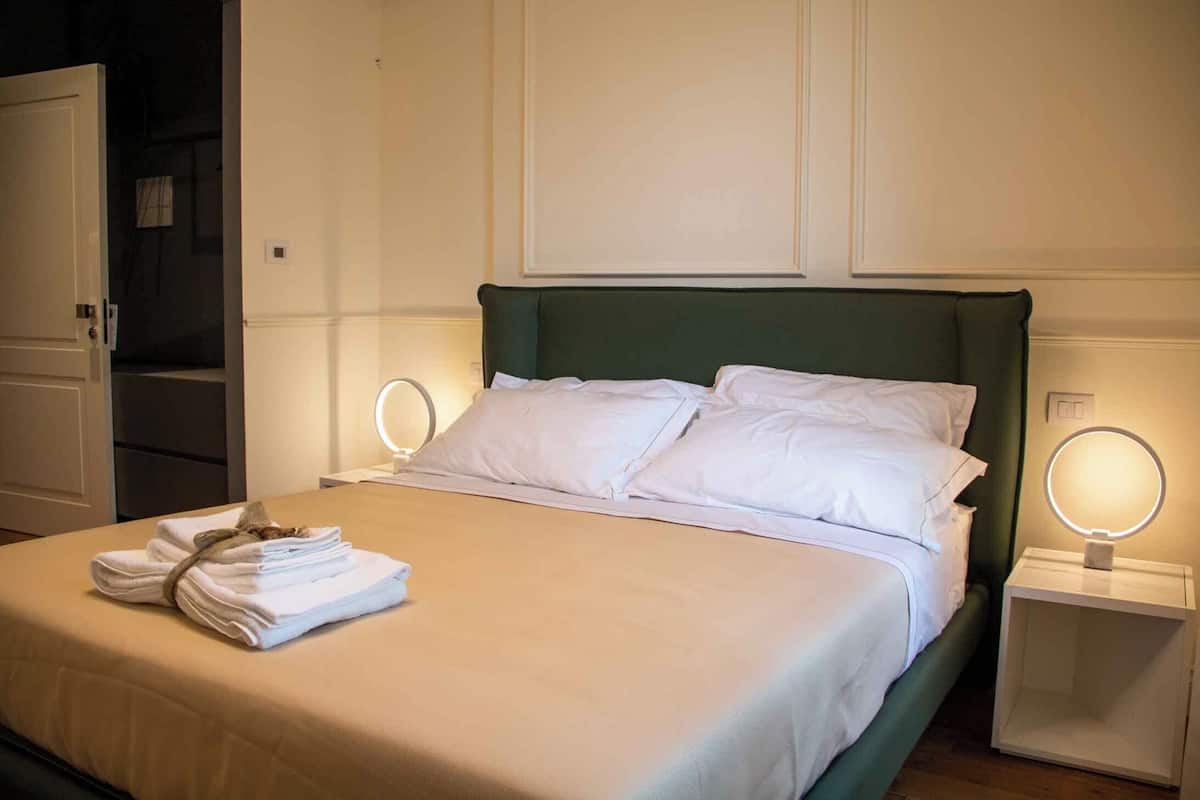 A neatly made bed with white linens and towels, two bedside tables with illuminated lamps, and a green headboard.