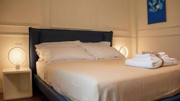A neatly made bed with white linens, two bedside tables with illuminated lamps, and a blue abstract painting on the wall.