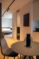 Ein modernes Hotelzimmer mit einem runden Esstisch, zwei Stühlen, einem Bett, einem Badezimmer und einer Küchenzeile.