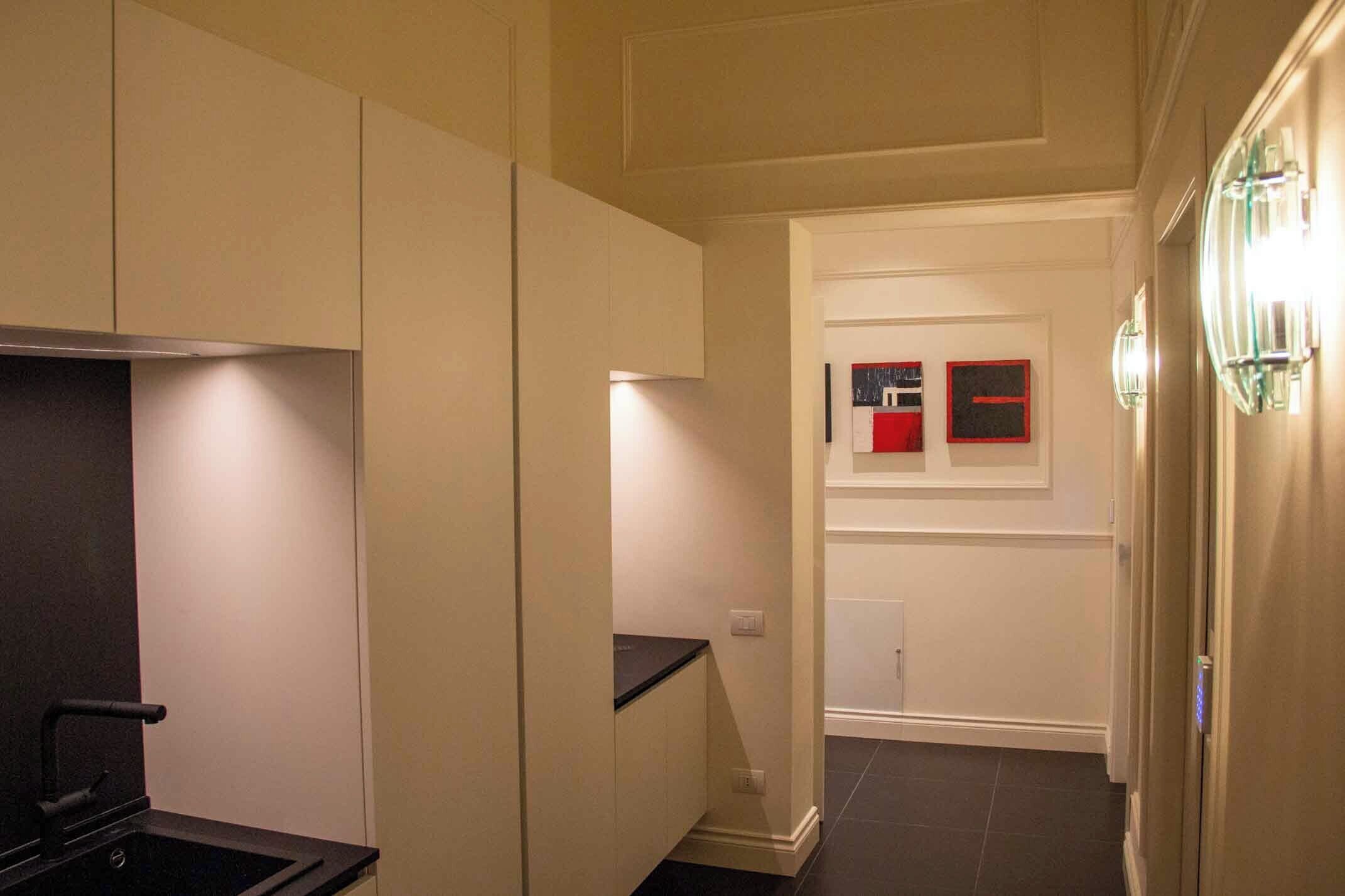 A narrow hallway with a kitchen area on the left, featuring cabinets and a black countertop.