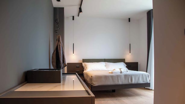 Une chambre d’hôtel moderne au design minimaliste, comprenant un lit avec du linge de lit blanc, une table de chevet et une petite table de nuit.