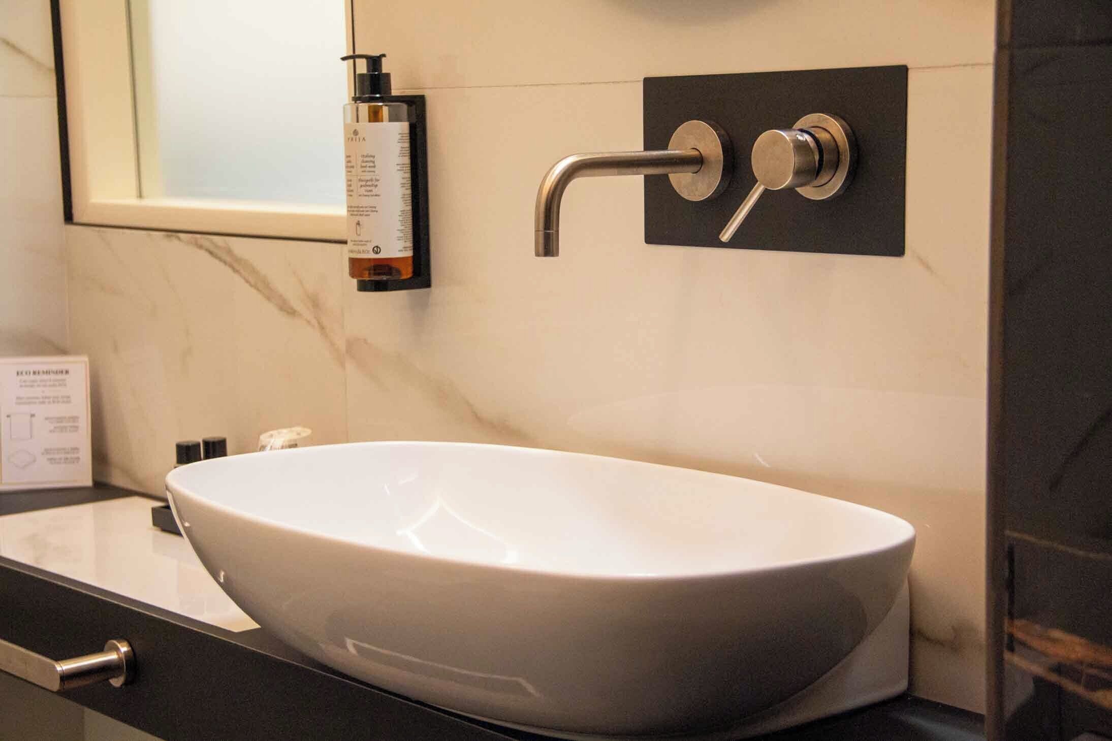 Ein modernes Badezimmer mit einem weißen Waschtischbecken, einer schwarzen Armatur und einer Handseifenflasche an der Wand.