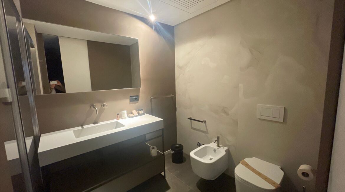 Ein Badezimmer mit Waschbecken, Spiegel und Bidet. An der Wand ist ein Handtuchhalter angebracht und es gibt eine Toilette mit einem Papierhandtuchhalter.