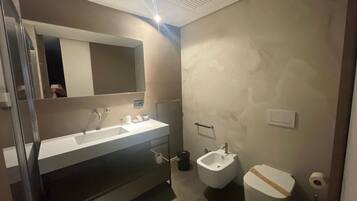 Ein Badezimmer mit Waschbecken, Spiegel und Bidet. An der Wand ist ein Handtuchhalter angebracht und es gibt eine Toilette mit einem Papierhandtuchhalter.