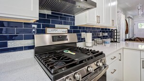A modern kitchen with white cabinets, a stainless steel range hood, and a blue-tiled backsplash.