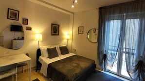 Un dormitorio con cama, mesita de noche, escritorio y ventana con cortinas.