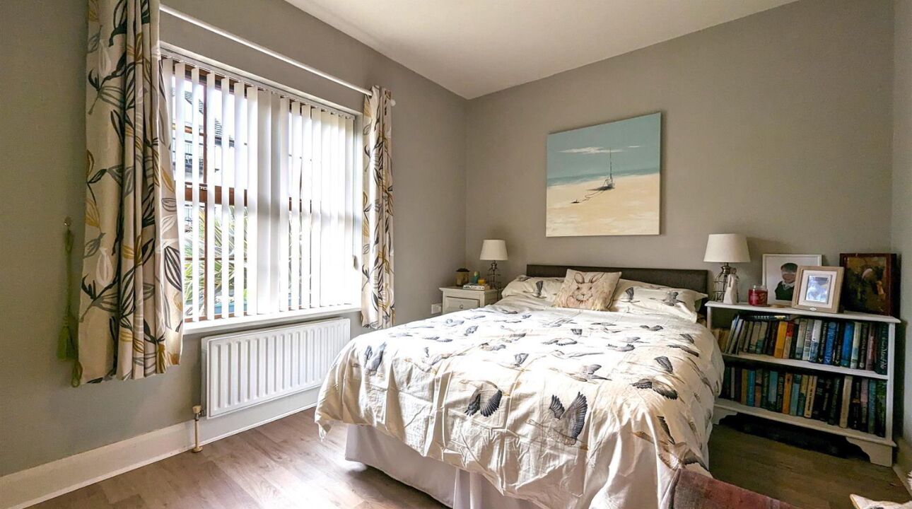 Ein Schlafzimmer mit einem großen Bett, einem Bücherregal, einem Heizkörper und einem Fenster mit Vorhängen.