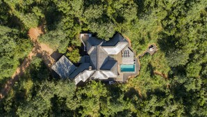 Eine Vogelperspektive eines Hauses, das von dichtem Wald umgeben ist, mit einem Schwimmbad, einer Terrasse und einer großen Holzterrasse.