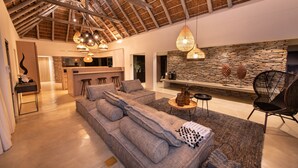 A spacious living area with a high ceiling, a stone fireplace, and a modern kitchen in the background. - Villa Aloe Vera in Hoedspruit (Hoedspruit)