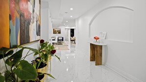 A modern hallway with a marble floor, a wooden side table with a vase of flowers, and a large abstract painting on the wall. - Caledon Escape I 7BR Home with BBQ & Backyard (Caledon)