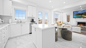 A spacious kitchen with white cabinetry, a marble island, and a large TV mounted above a fireplace. - Caledon Escape I 7BR Home with BBQ & Backyard (Caledon)