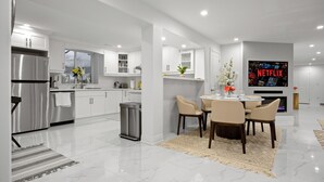 A modern kitchen with white cabinetry, a stainless steel refrigerator, and a dining area with a table and chairs. - Caledon Escape I 7BR Home with BBQ & Backyard (Caledon)