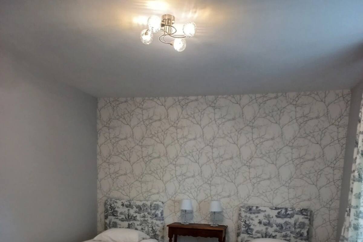 Une chambre avec deux lits simples, une petite table de chevet en bois avec deux lampes et une chaise bleue.