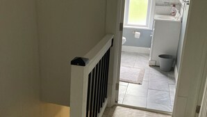 Een gang die leidt naar een badkamer met een raam, een wastafel en een toilet.