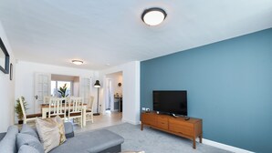 Una sala de estar moderna con un sofá gris, un mueble bajo para televisión de madera y una pared azul de acento.