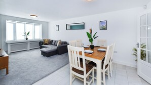 Una sala de estar moderna con un sofá gris, una mesa de comedor con sillas blancas y un ventanal con vistas.
