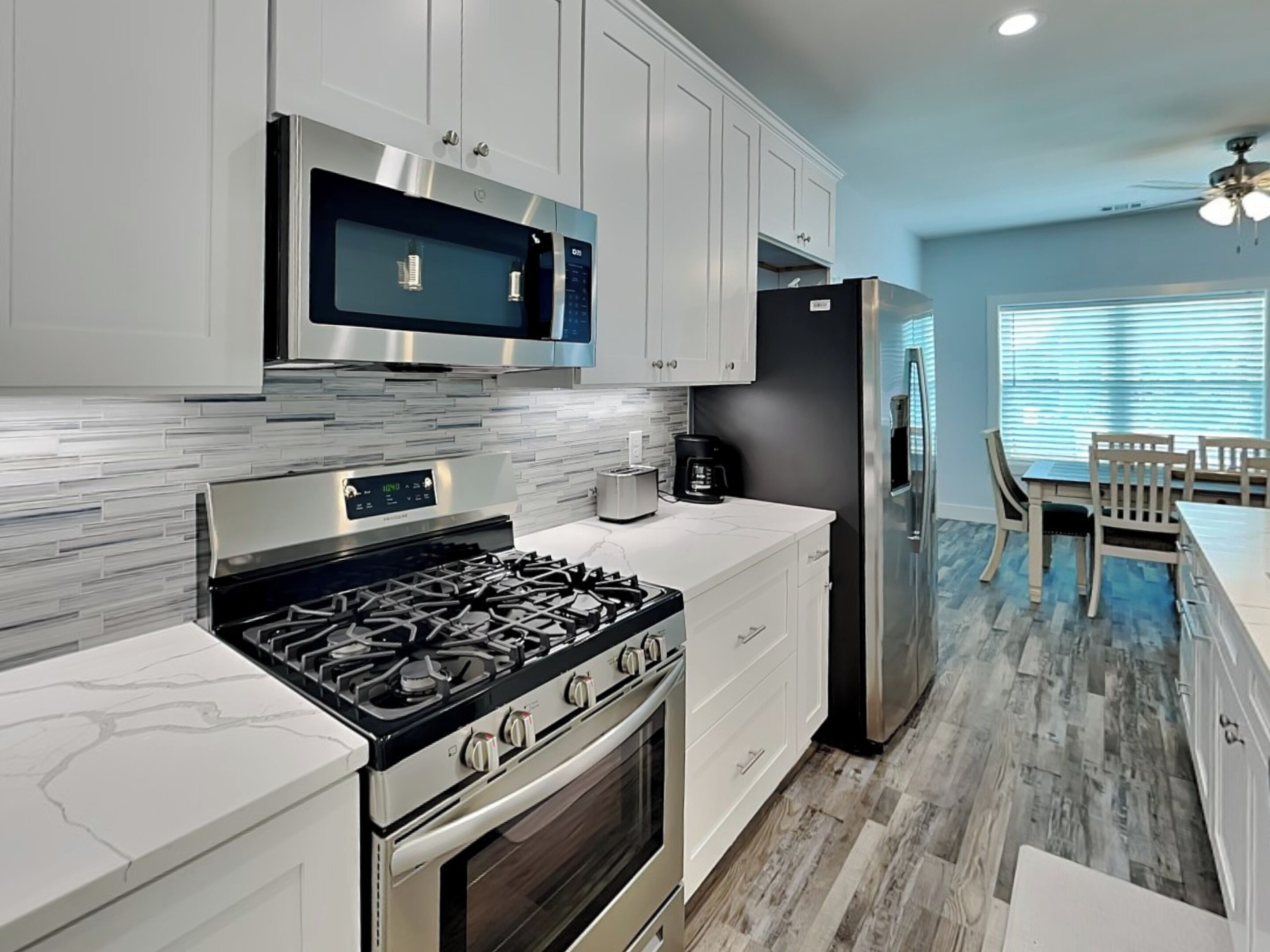A modern kitchen with stainless steel appliances, white cabinetry, and a marble countertop.