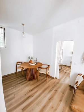A room with a wooden floor, a round table with chairs, a hanging light fixture, and a doorway leading to another room. - Casa SaloYa (Sintra)