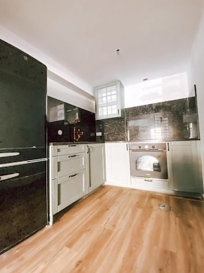 A kitchen with a wooden floor, white cabinets, a black countertop, and a stainless steel oven. - Casa SaloYa (Sintra)