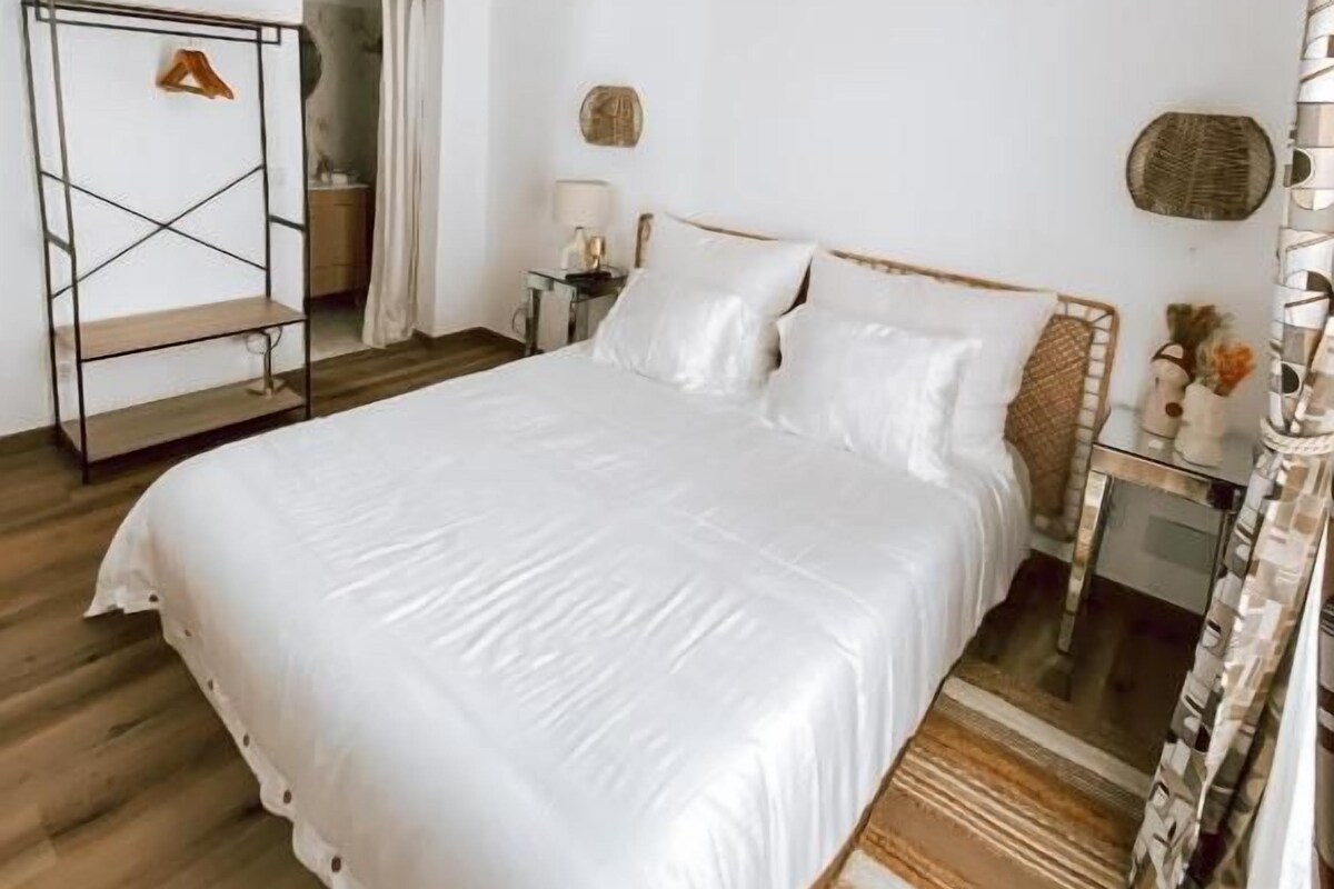 A bedroom with a large bed, a ceiling fan, a bedside table with a lamp, and a small rug.