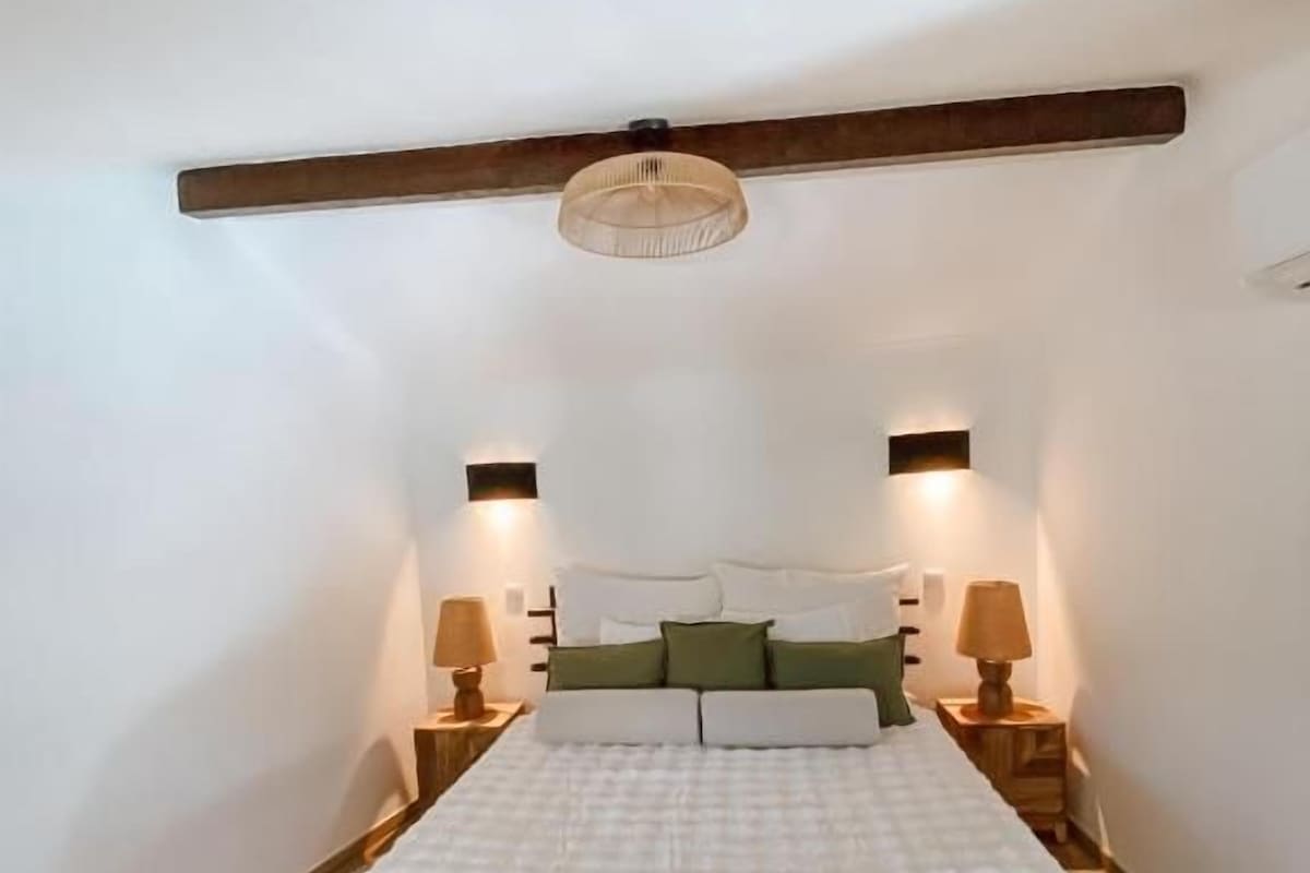 A bedroom with a large bed, two bedside lamps, and a wooden beam ceiling.