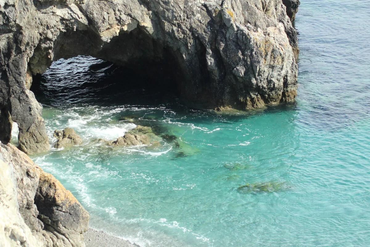 A rocky coastal area with clear turquoise water and a cave entrance.