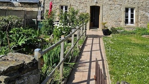 A stone building with a wooden pathway leading to the entrance, surrounded by greenery. - Stone house 600 m from the sea with garden and terrace. (Plomodiern)