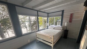 Ein Schlafzimmer mit Bett, großen Fenstern und Blick auf Bäume.