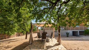 Eine Terrasse im Freien mit Steinboden, einem Tisch und Stühlen sowie einer Pergola, die Schatten spendet.